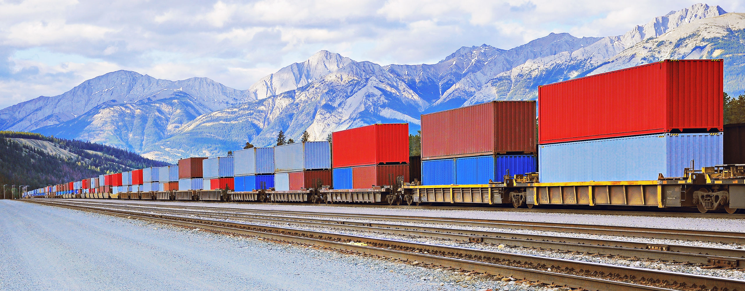 Blue and red Accurate Logistics USA container shipments being transported over rail in front of mountains