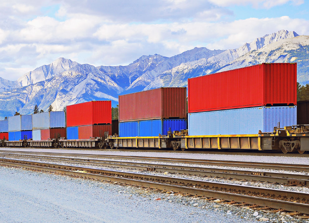 Blue and red Accurate Logistics USA container shipments being transported over rail in front of mountains